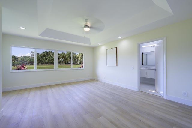 unfurnished bedroom with baseboards, a ceiling fan, a tray ceiling, light wood-type flooring, and recessed lighting