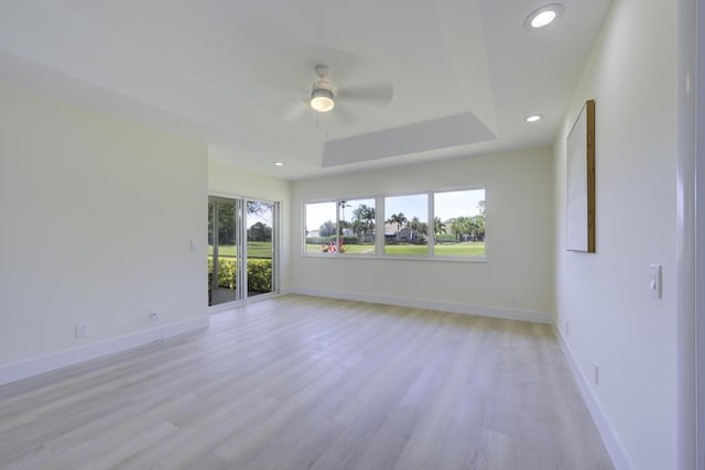 empty room with baseboards, ceiling fan, light wood-style flooring, a tray ceiling, and recessed lighting