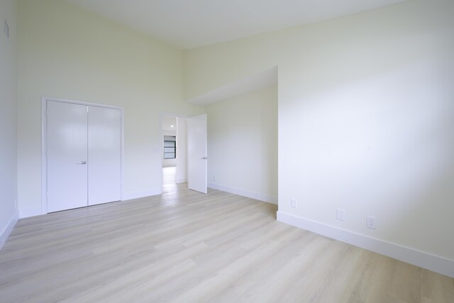 unfurnished bedroom featuring a high ceiling, a closet, light wood-style flooring, and baseboards