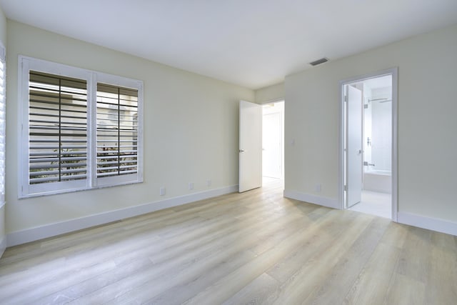 unfurnished bedroom featuring baseboards, ensuite bathroom, visible vents, and light wood-style floors