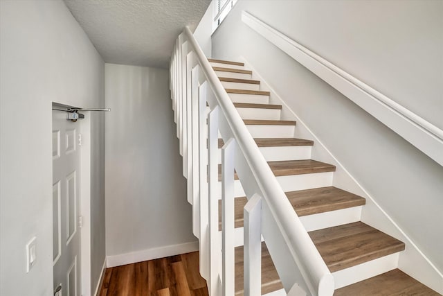 staircase featuring a textured ceiling, baseboards, and wood finished floors