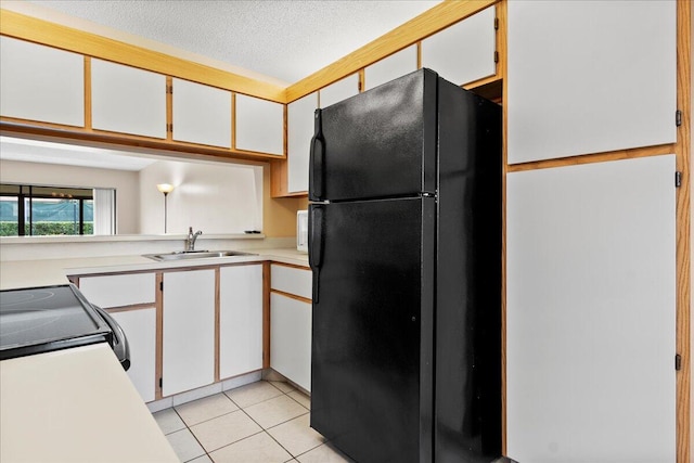 kitchen with light tile patterned floors, white cabinets, light countertops, black appliances, and a sink