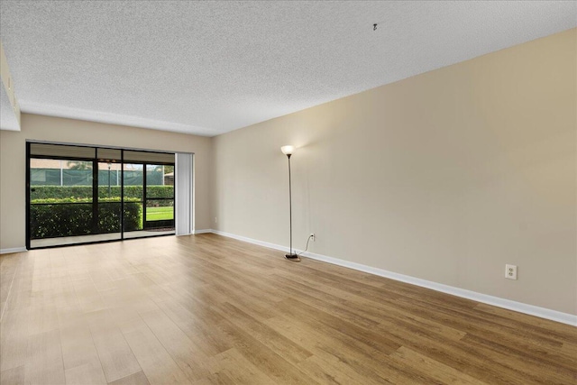 spare room featuring a textured ceiling, light wood-style flooring, and baseboards