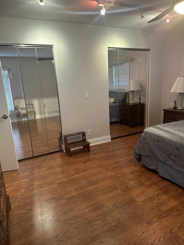 bedroom with multiple closets, ceiling fan, wood-type flooring, and a textured ceiling