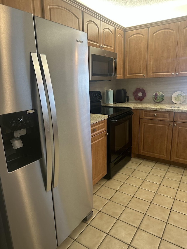 kitchen with tasteful backsplash, light stone countertops, light tile patterned flooring, and appliances with stainless steel finishes