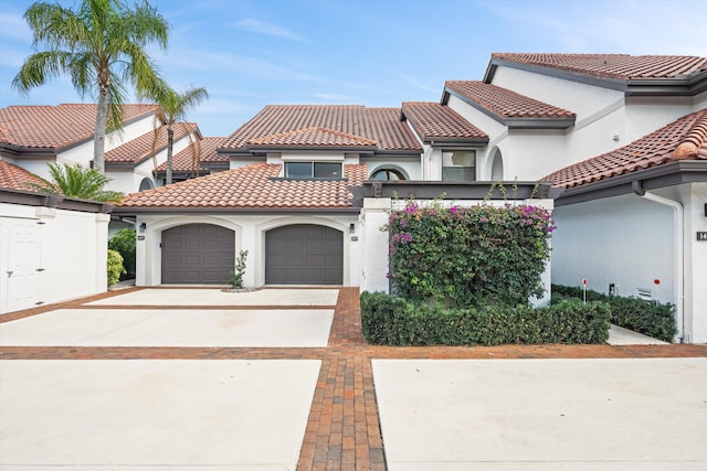 mediterranean / spanish-style home with a garage, driveway, a tiled roof, and stucco siding