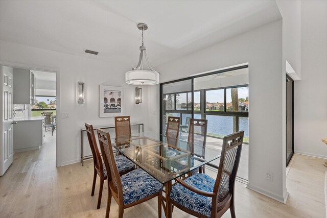 dining room with a water view, light wood finished floors, visible vents, and baseboards