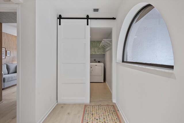 hall featuring a barn door, visible vents, baseboards, light wood-type flooring, and washer / clothes dryer