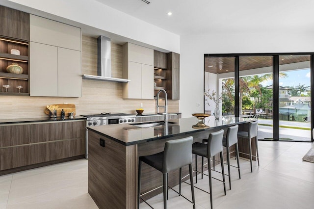 kitchen with a sink, wall chimney range hood, open shelves, an island with sink, and modern cabinets