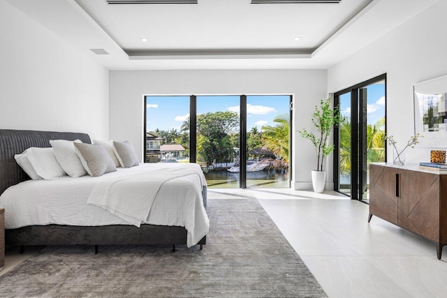 bedroom with access to exterior, a tray ceiling, and multiple windows