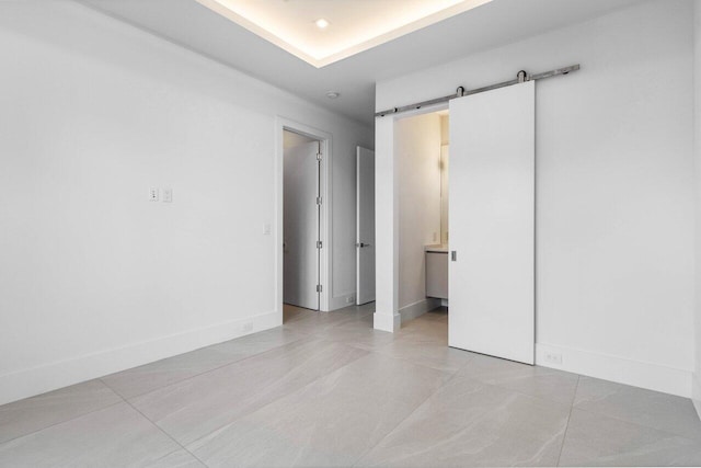 unfurnished room with light tile patterned floors, baseboards, and a barn door