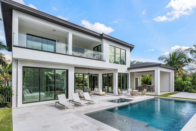 rear view of property featuring a balcony, a patio area, a pool with connected hot tub, and stucco siding