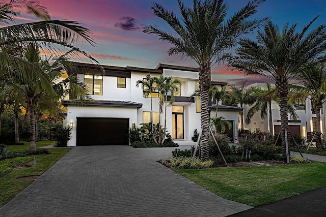 modern home featuring a yard, decorative driveway, an attached garage, and stucco siding