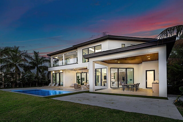 back of property at dusk featuring a balcony, a patio area, and stucco siding