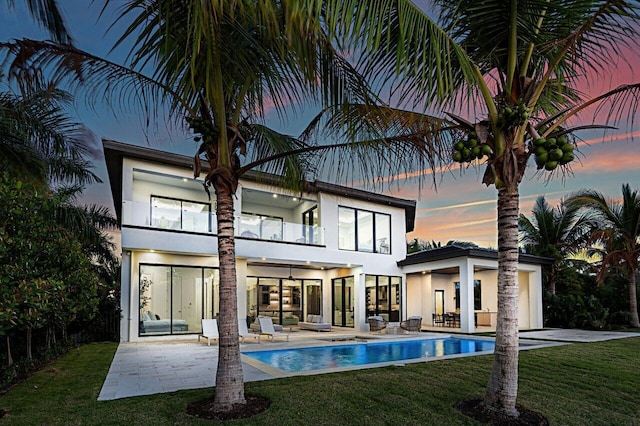 back of property at dusk with ceiling fan, a patio, a balcony, a yard, and stucco siding