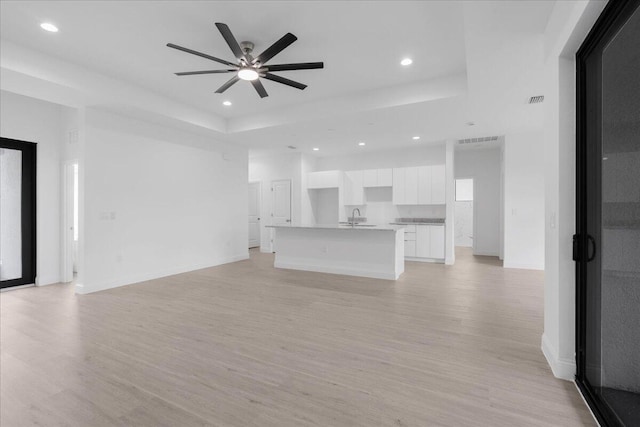 604 Lake Ave, Lehigh Acres, FL 33972 - unfurnished living room featuring sink, a raised ceiling, ceiling fan, and light hardwood / wood-style flooring