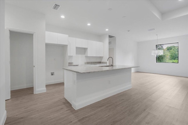 604 Lake Ave, Lehigh Acres, FL 33972 - kitchen featuring sink, light stone counters, white cabinetry, decorative light fixtures, and light hardwood / wood-style floors