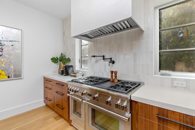 kitchen featuring range with two ovens, custom range hood, backsplash, and light hardwood / wood-style floors