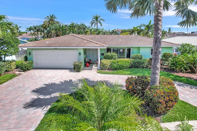 view of front of house with an attached garage, fence, a tile roof, decorative driveway, and stucco siding