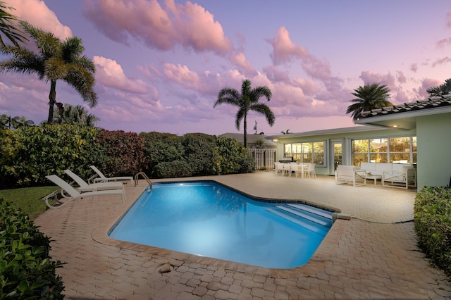 pool at dusk featuring a patio and outdoor lounge area