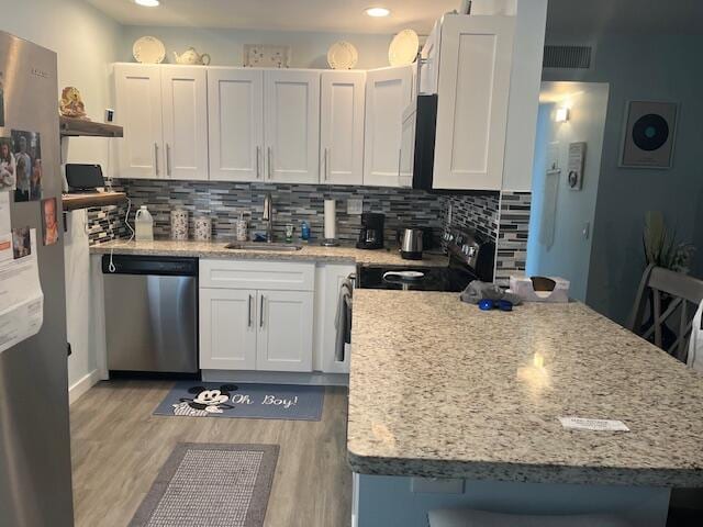 kitchen featuring tasteful backsplash, light wood-style flooring, stainless steel appliances, white cabinetry, and a sink