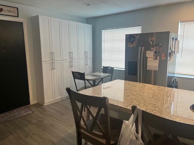 kitchen with dark wood-style floors, a healthy amount of sunlight, stainless steel refrigerator with ice dispenser, and light stone countertops