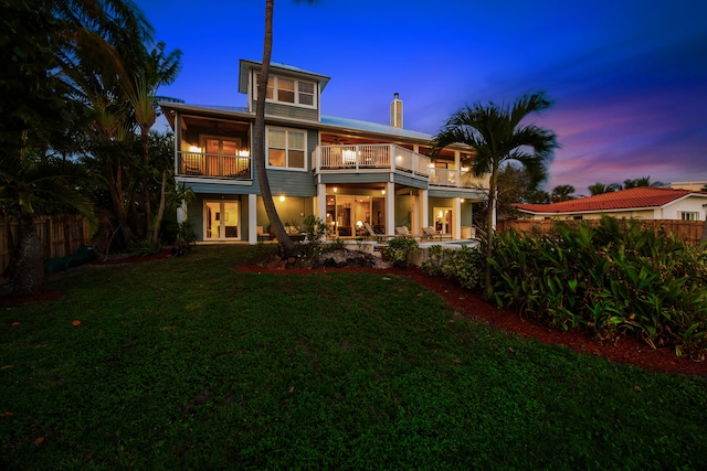 back house at dusk with a yard and a balcony