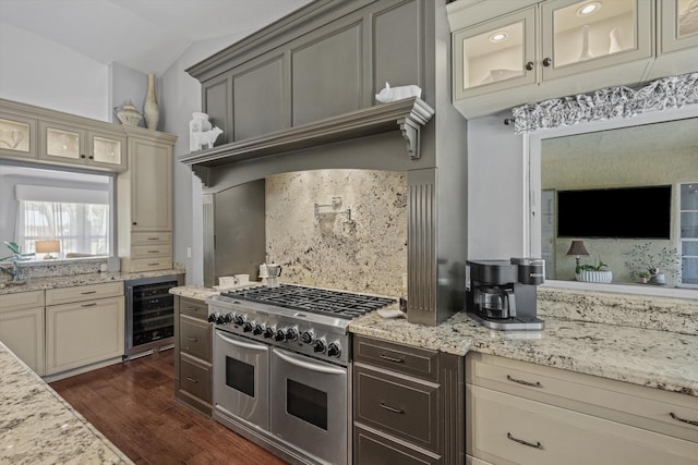 kitchen featuring cream cabinets, double oven range, tasteful backsplash, light stone counters, and beverage cooler