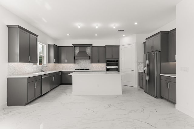 kitchen with marble finish floor, wall chimney range hood, appliances with stainless steel finishes, backsplash, and a center island