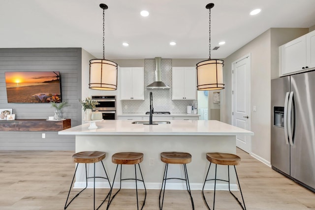 kitchen featuring stainless steel appliances, wall chimney range hood, a kitchen bar, and light wood-style floors