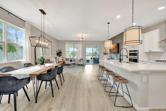 kitchen featuring a breakfast bar, tasteful backsplash, light countertops, light wood-style floors, and a sink