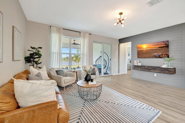 living room with wooden walls, visible vents, an accent wall, wood finished floors, and a chandelier