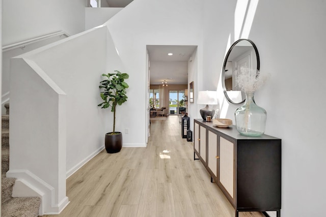 hallway with stairs, light wood-type flooring, a towering ceiling, and baseboards