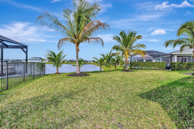 view of yard with glass enclosure, a water view, and fence