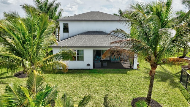 rear view of property featuring roof with shingles, a lawn, and stucco siding