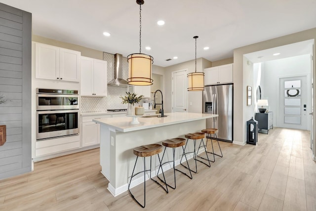 kitchen featuring white cabinets, stainless steel appliances, light wood-type flooring, wall chimney range hood, and a sink