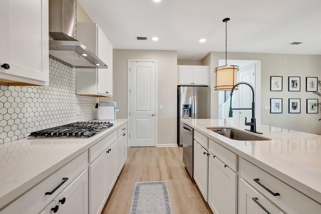 kitchen featuring stainless steel appliances, a sink, visible vents, light countertops, and wall chimney range hood