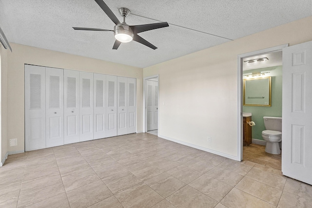 unfurnished bedroom with connected bathroom, a textured ceiling, baseboards, and a ceiling fan