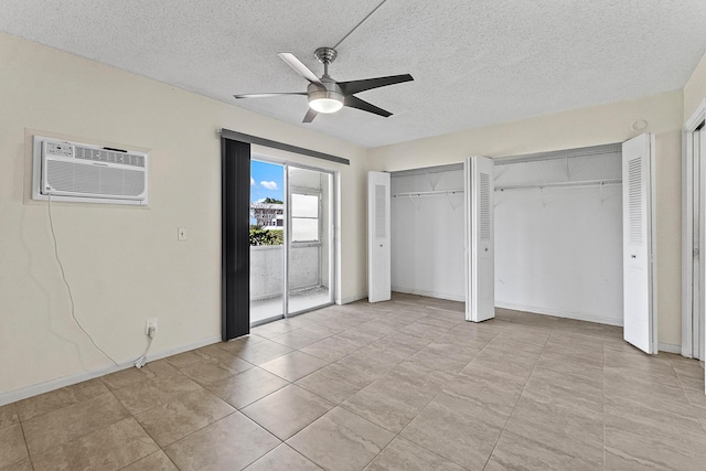 unfurnished bedroom with two closets, a textured ceiling, a wall unit AC, baseboards, and ceiling fan