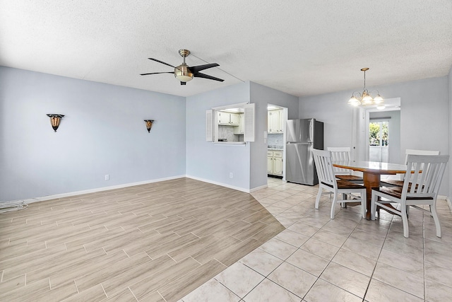 dining area with baseboards, light wood finished floors, a textured ceiling, and ceiling fan with notable chandelier