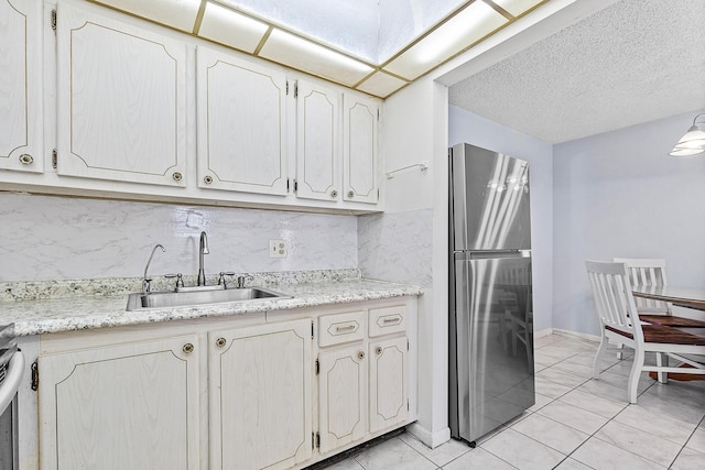 kitchen featuring decorative backsplash, light countertops, freestanding refrigerator, and a sink