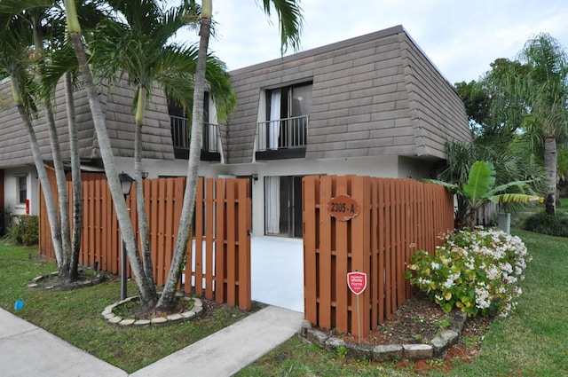 view of side of home with fence, a lawn, a balcony, and mansard roof