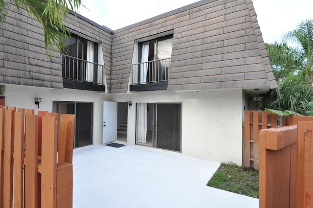 back of property with fence, mansard roof, a patio, and stucco siding