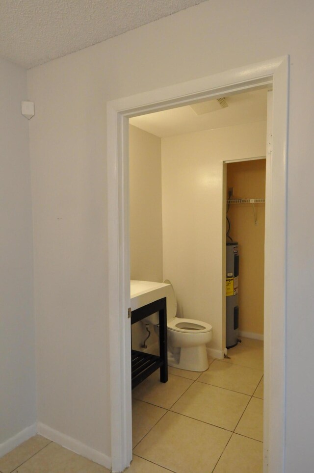 empty room featuring a textured ceiling, light tile patterned floors, a ceiling fan, and baseboards