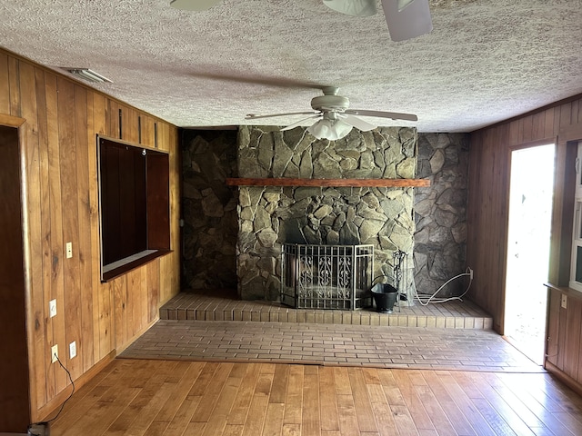 unfurnished living room featuring a fireplace, hardwood / wood-style flooring, wooden walls, and ceiling fan