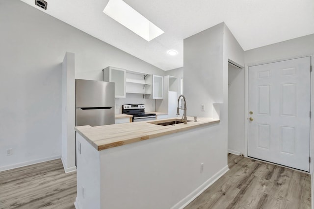 kitchen featuring open shelves, light wood-type flooring, a peninsula, stainless steel appliances, and a sink