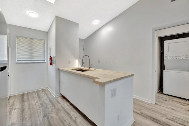 kitchen featuring butcher block countertops, light wood-type flooring, a peninsula, stacked washer / drying machine, and a sink