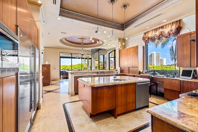 kitchen with a raised ceiling, an island with sink, hanging light fixtures, and crown molding