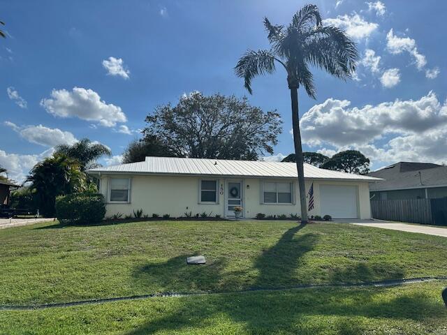 ranch-style home with metal roof, an attached garage, concrete driveway, stucco siding, and a front lawn