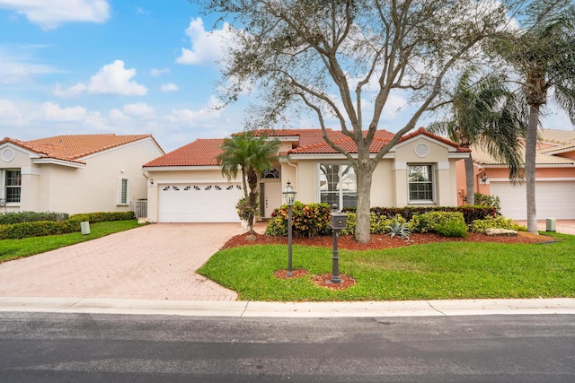 mediterranean / spanish home featuring an attached garage, a tiled roof, decorative driveway, stucco siding, and a front yard